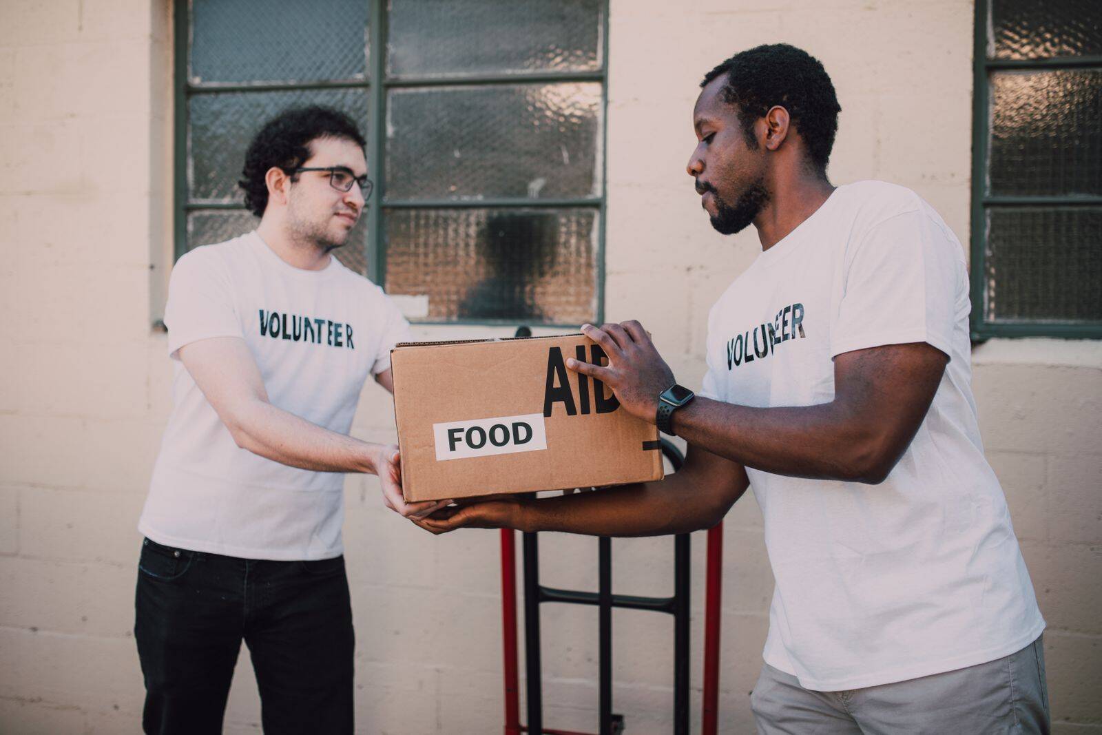 Two volunteers hand over an aid box marked 'FOOD' outside, promoting community service.